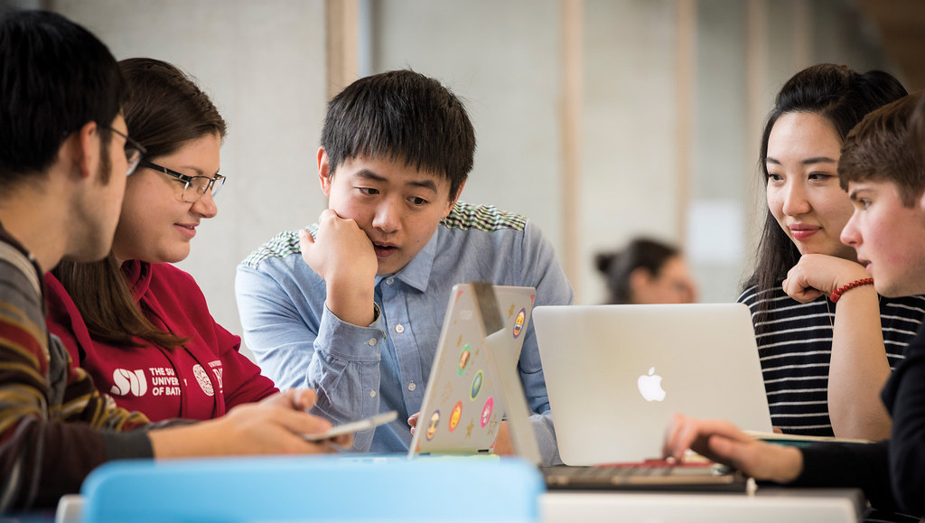 Group of five students working on laptops and smartphone.