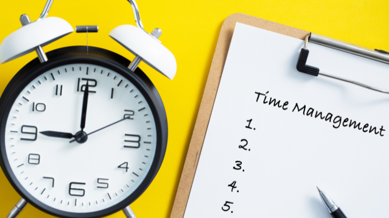 A sheet of paper on a clipboard has the title 'Time management' followed by a numbered list. There's a big alarm clock next to the clipboard.