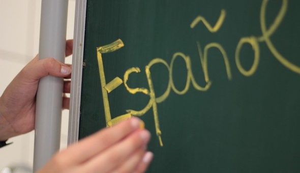 A teacher writes 'Espanol' in yellow chalk on a blackboard.