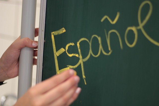 A teacher writes 'Espanol' in yellow chalk on a blackboard.