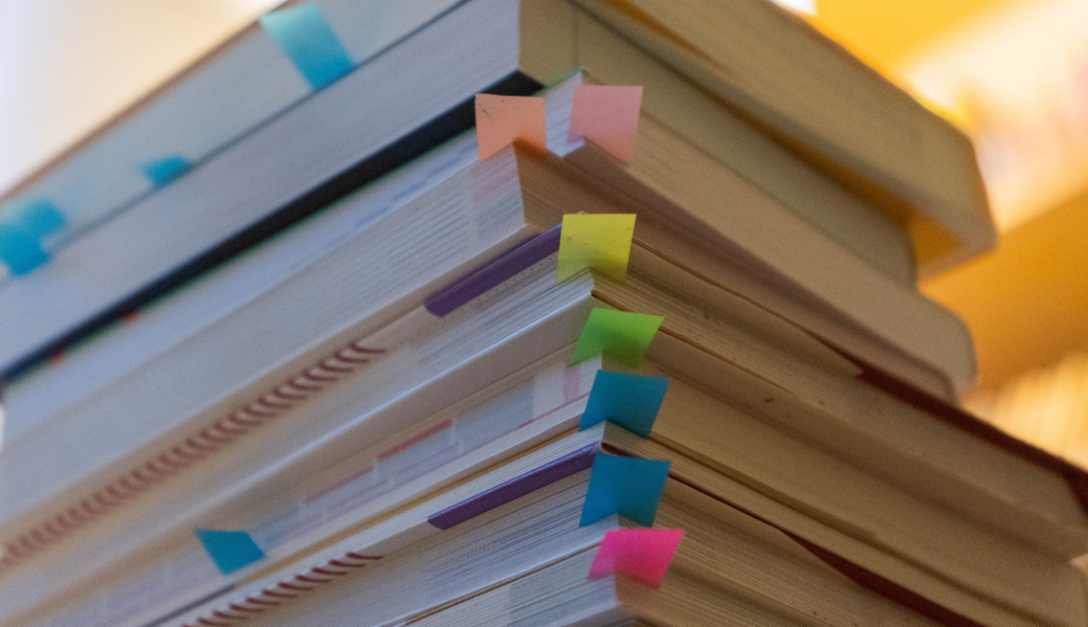 Pile of text books with coloured sticky labels attached to some pages.
