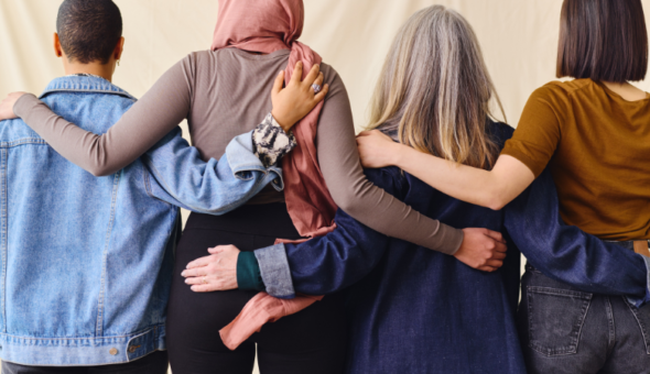 Rear portrait of four women standing in a line with their arms around each other.