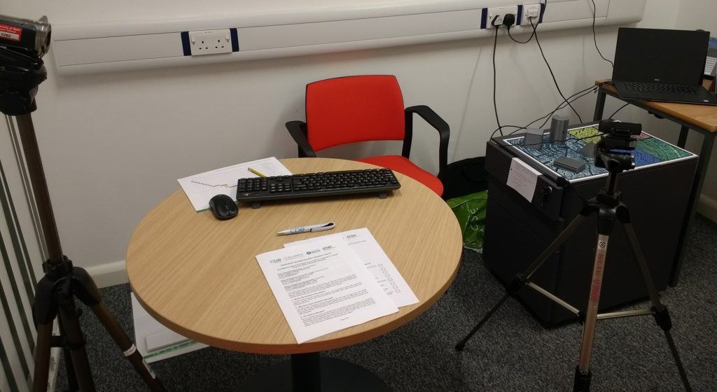 The setup of the room for the next study in my AR for Dementia project. There is a table with information sheets next to a board with grey objects. A camera and laptop screen can be seen near the objects.