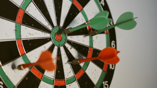 A dartboard with four darts, one of which has hit the bullseye.