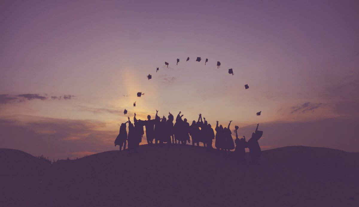 Graduates in the distance throwing their caps in to the air at sunset.