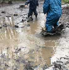 Small children in waterproofs play in the mud.