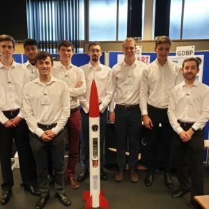 Eight mechanical and integrated mechanical and electrical engineers of the 2020 team posing besides their rocket model.