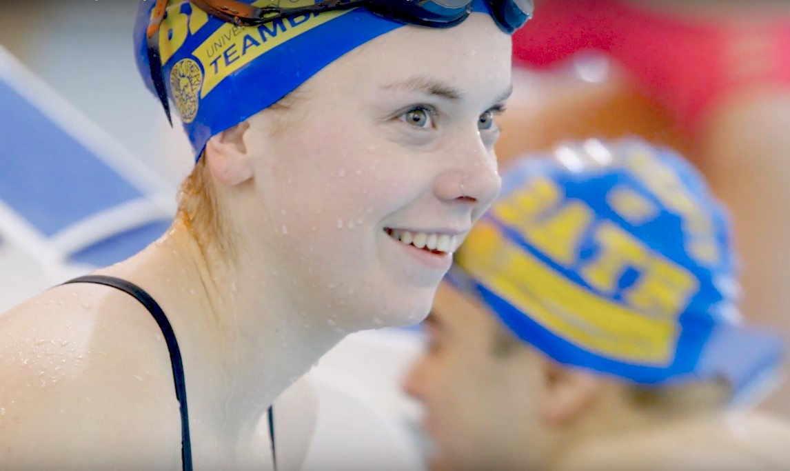 A smiling female swimmer in the pool wearing a Team Bath swimming hat.