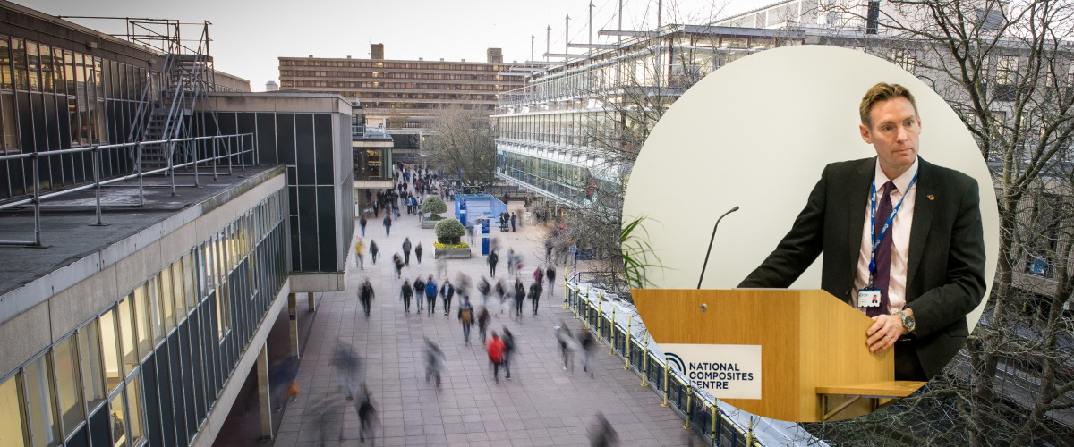 A man in a suit standing behind a lectern against of backdrop of the University of Bath Parade street.
