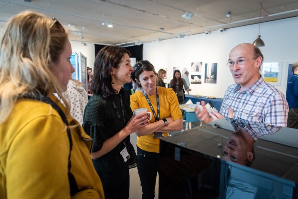 A Caucasian man in a patterned short is talking to a group of three women who are smiling and laughing.