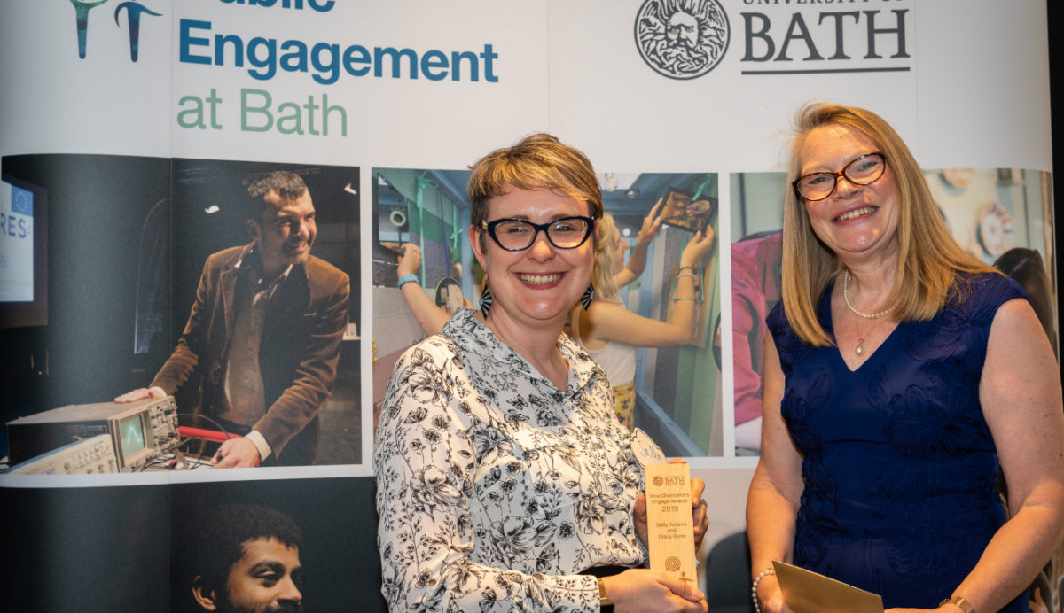 An award winner holding their trophy in front of a banner that says Public Engagement at Bath