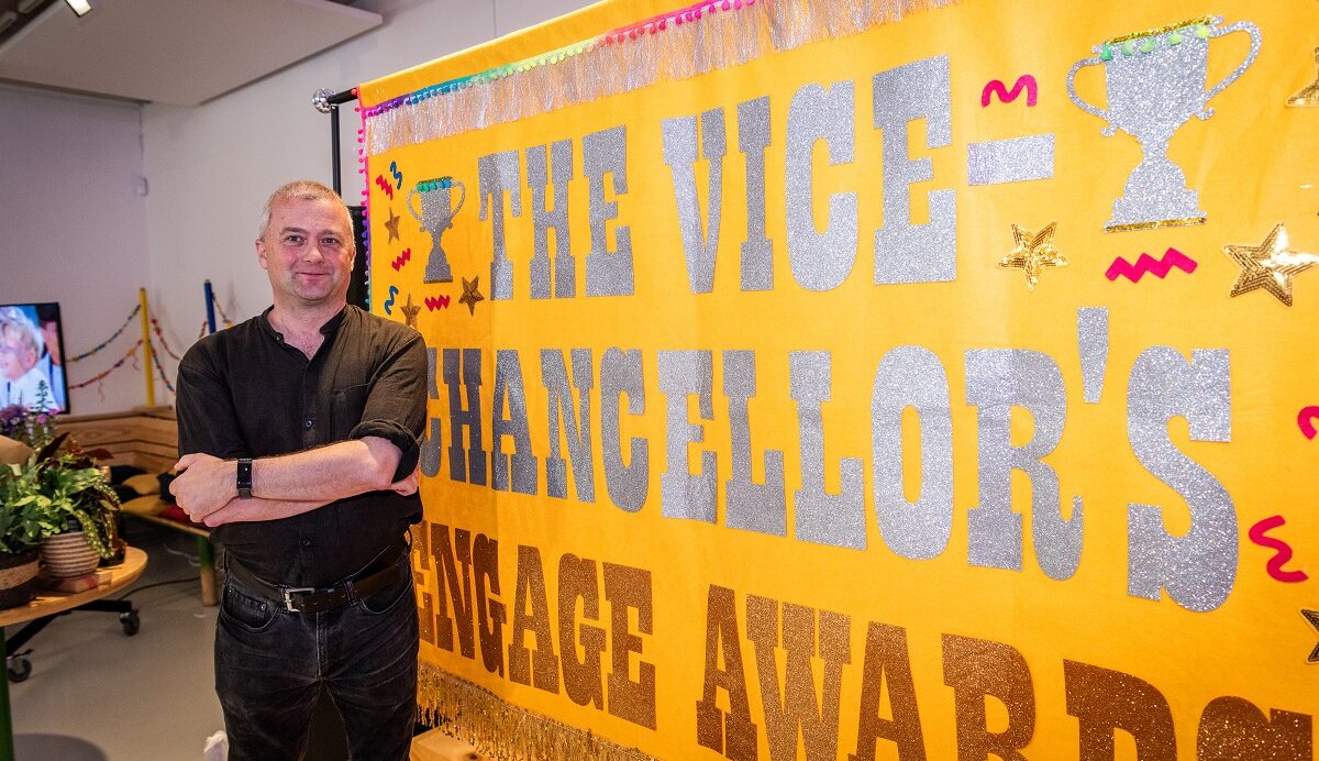 A white man stands in front of a large banner that says the words 'Vice-Chancellor's Engage Awards'