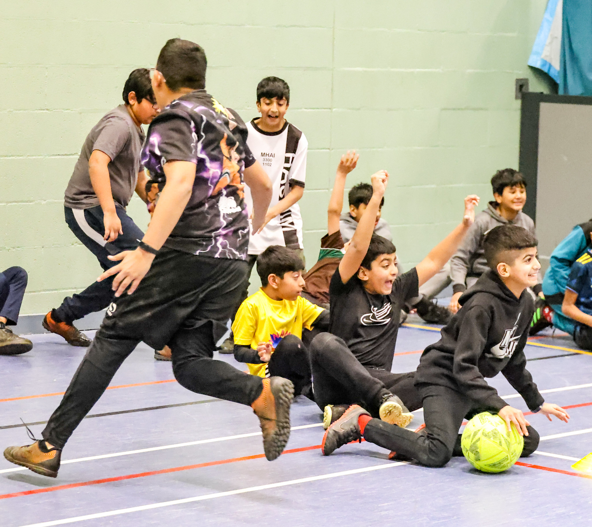 A group of young people celebrate during a ball-game in a sports hall.