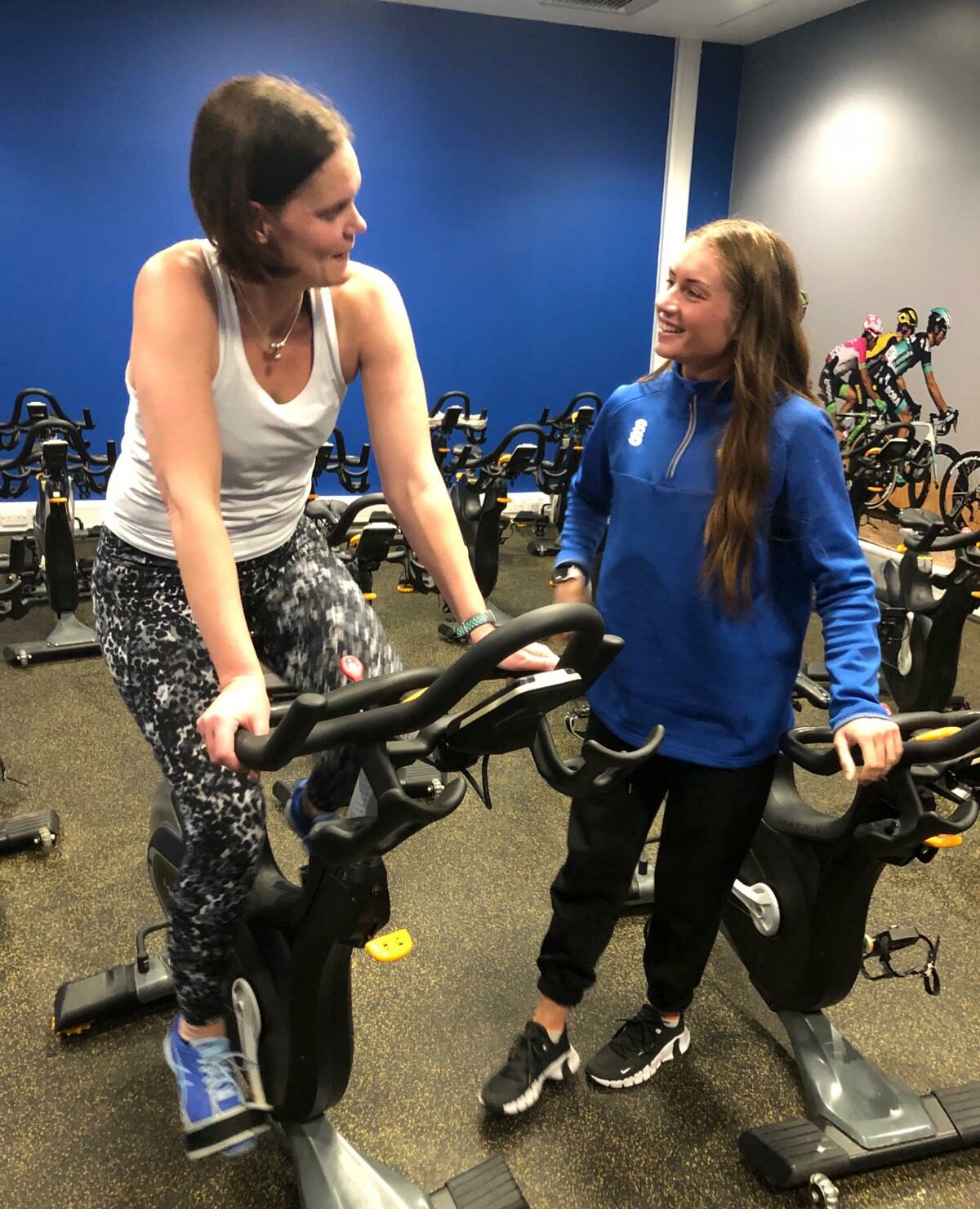 Cassie Wilson on an exercise bike speaking to a gym instructor