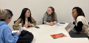 Five students sitting around a table and talking at a PGT Writing Café 