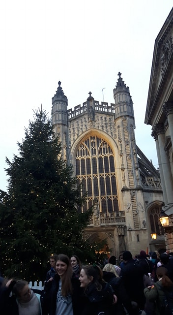 A Christmas tree outside Bath Abbey with people passing by