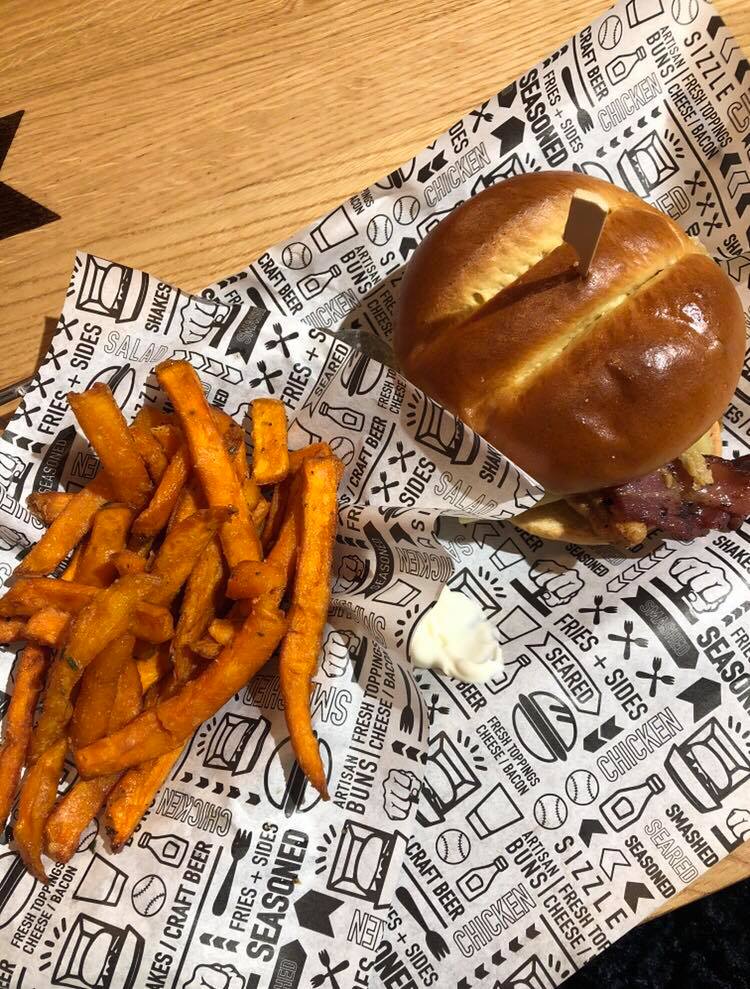 A burger with some chips on the side on 'fake' newspaper