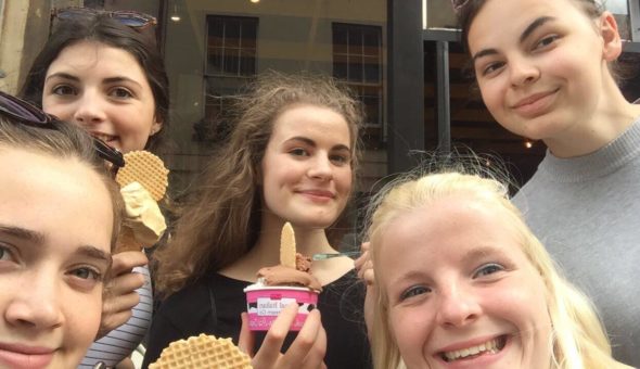 Marnie holding an ice cream scope and wafer in a pink tub. She is surrounded by three other female students - most of the face of a blond haired girl is visible but you can't see most of the other two girls