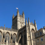Picture of a sand-stone coloured church, called the Bath Abbey, against a blue sky.