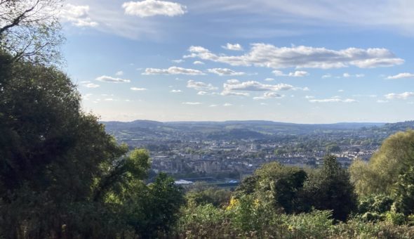 View of Bath from mountain top, surrounded by grass, trees and hills.