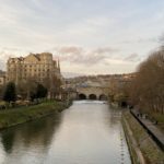 Picture of a bridge and buildings in the distance with a calming river flowing underneath it.