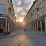 A cobble stone street with tall, columned buildings on either side of it.