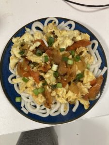 A plate of noodles with eggs and tomatoes on top.