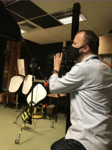 Male in photography studio sat on stool and looking through camera.
