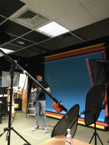 View through boom in photography studio of male student in front of blue screen.