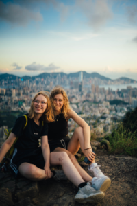 2 students on a hilltop with the city of Hong Kong in the background