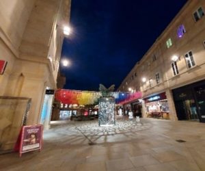 A view of Bath's Southgate shopping centre with some colourful rainbow decorations between the buildings