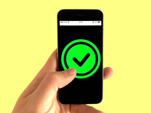 Black phone with a large line green circle with a thin black border and black tick on a bright yellow background